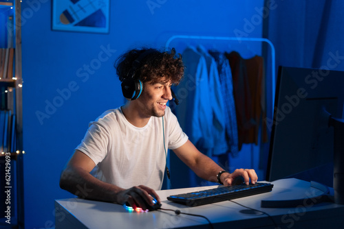 Happy young arabic gamer wearing headphones playing video game on personal computer, play in eSport cyber games tournament in neon light. © mtrlin