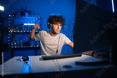 Angry arabic guy gamer showing fist and angry at losing game while playing video games at home on computer in neon light.