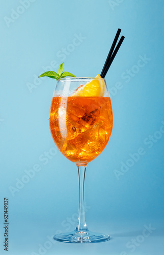glass of aperol spritz cocktail with straw on blue background