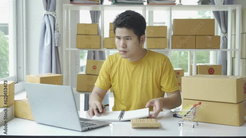 Asian young man selling online at home with box and laptop taking orders from customers, concept with SME business Asian young man selling online at home with box and laptop taking orders from customers, concept with SME business