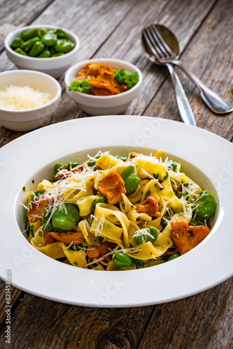 Tagliatelle with broad bean, chanterelle mushrooms and parmesan cheese on wooden table
