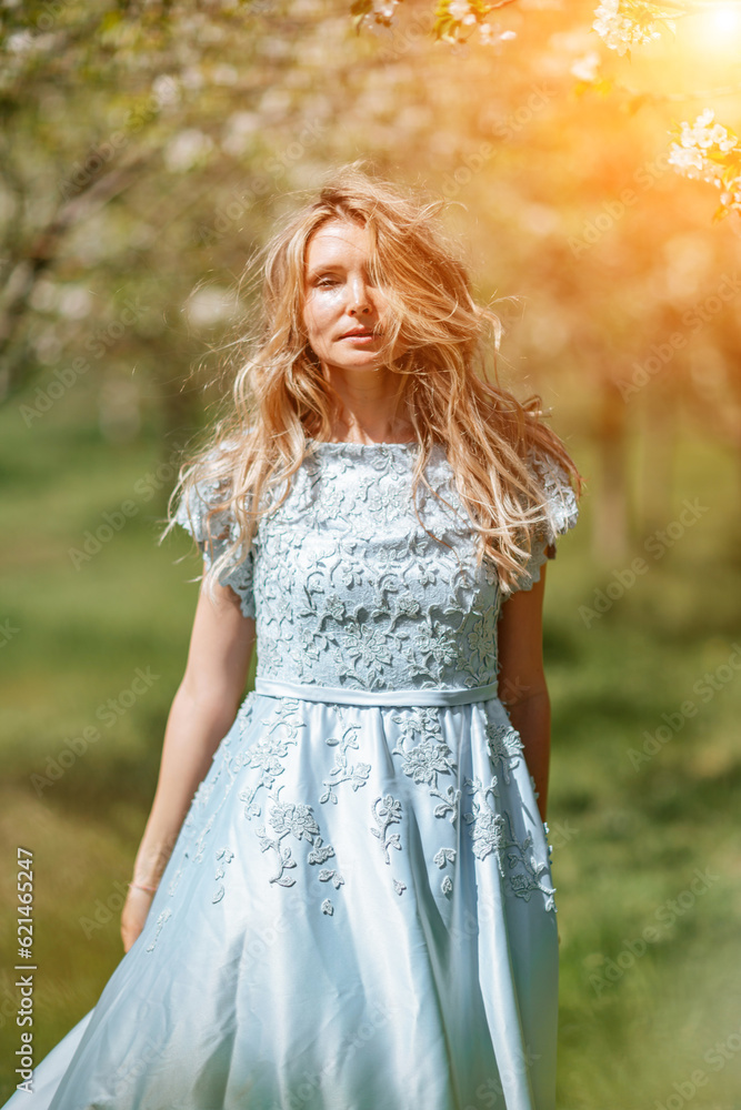 Blond blooming garden. Portrait of a blonde in the park. Happy woman with long blond hair in a blue dress. Blond blooming garden. Portrait of a blonde in the park. Happy woman with long blond hair in a blue dress.