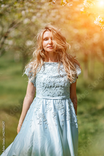 Blond blooming garden. Portrait of a blonde in the park. Happy woman with long blond hair in a blue dress.