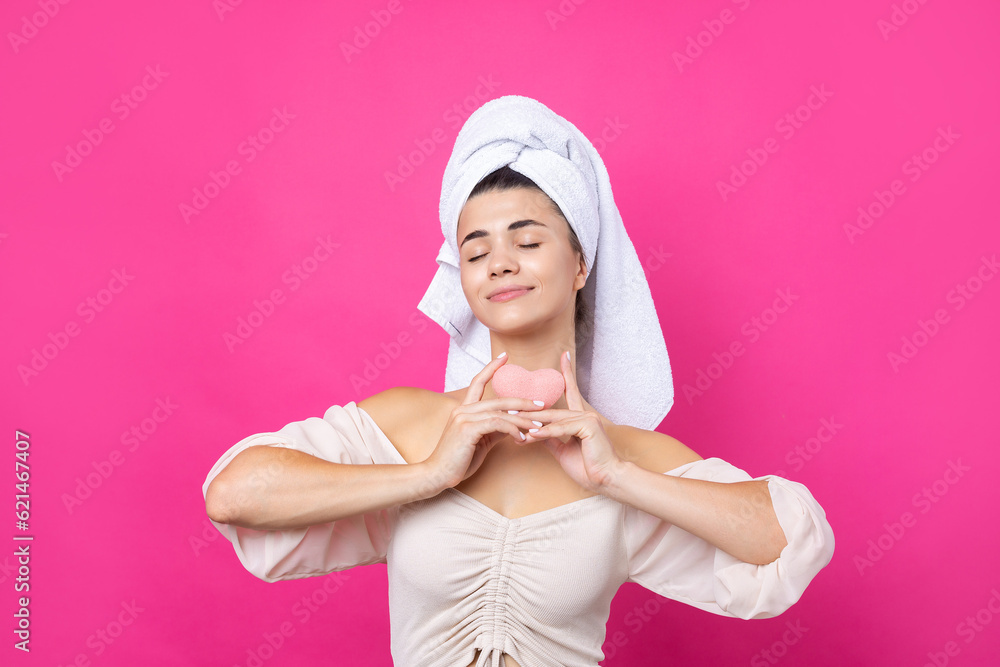 Beautiful cheerful attractive girl with a towel on her head, holds a sponge in the form of a pink heart. Beautiful cheerful attractive girl with a towel on her head, holds a sponge in the form of a pink heart.