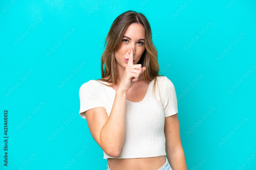 Young caucasian woman isolated on blue background showing a sign of silence gesture putting finger in mouth