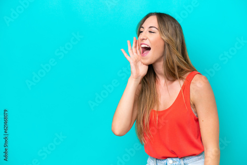 Young caucasian woman isolated on blue background shouting with mouth wide open to the side