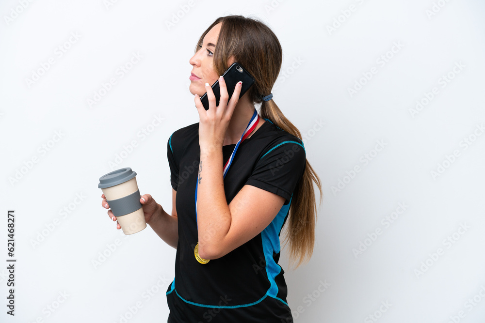Young caucasian woman with medals isolated on white background holding coffee to take away and a mobile Young caucasian woman with medals isolated on white background holding coffee to take away and a mobile