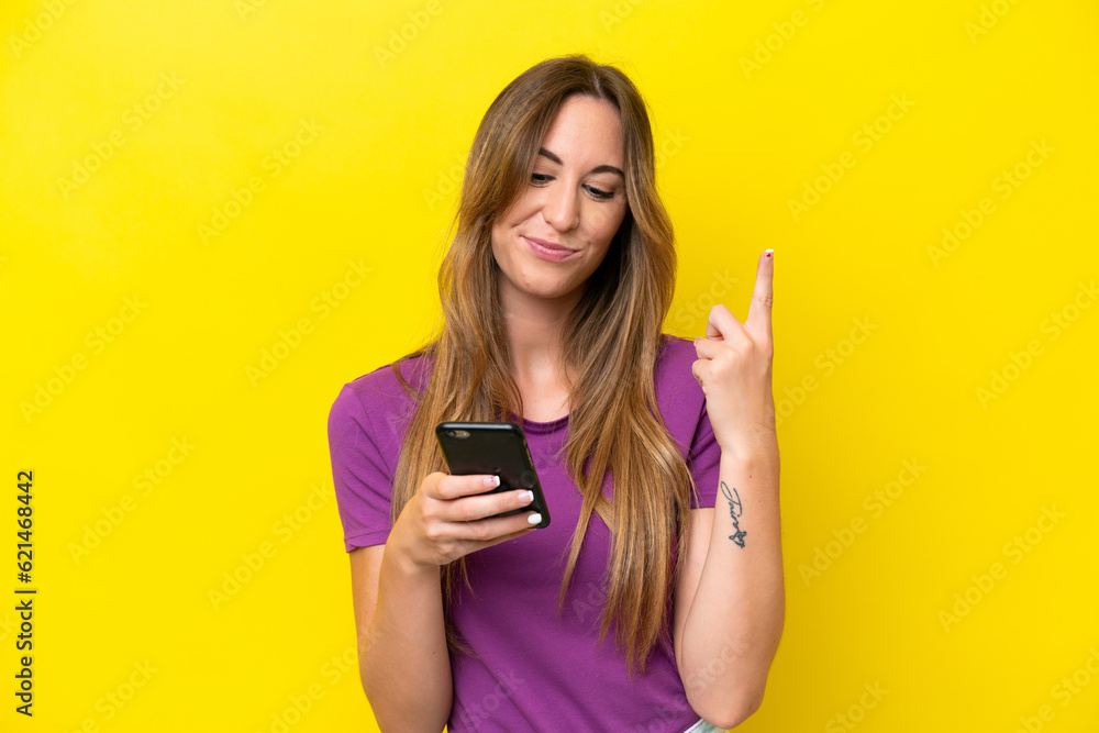 Young caucasian woman isolated on yellow background using mobile phone and lifting finger Young caucasian woman isolated on yellow background using mobile phone and lifting finger