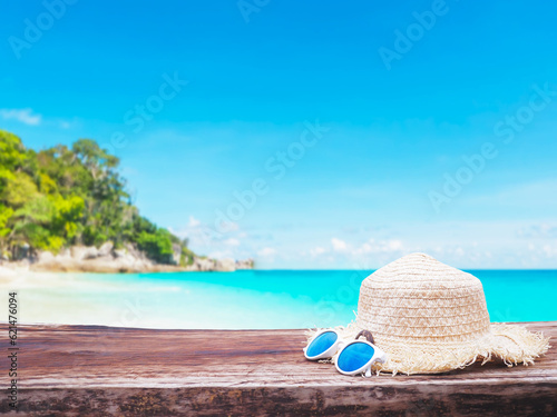 Close up straw hat and sunglasses on wooden table over summer beach background.