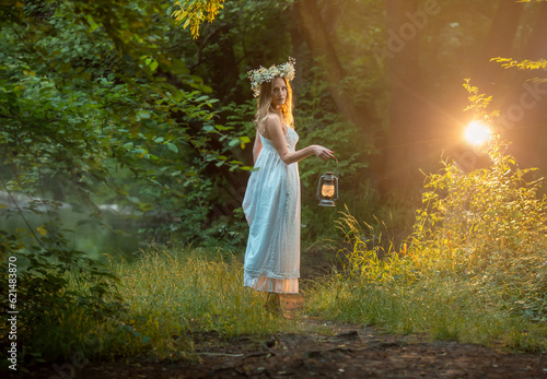 girl is standing in the forest an old kerosene lamp in her hands, with a wreath of daisies on her head.