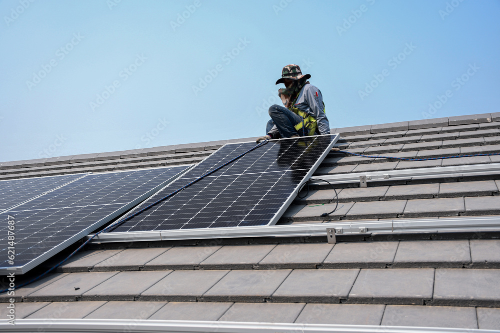 A technician is installing solar panels on the roof to use solar energy to power the building. A technician is installing solar panels on the roof to use solar energy to power the building.