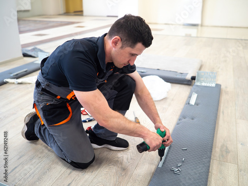 Man furniture assembler. Worker uses electric screwdriver. Guy furniture maker during work. Bed assembly process. Furniture store specialist in overalls. Man provides bed assembly services