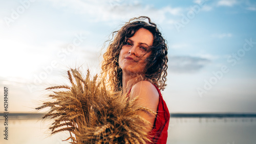 A curly girl in a red dress with ears of wheat in her hands