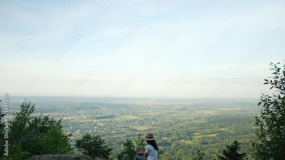 Back view of little girl child in hat sitting on big stone and enjoying amazing summer nature during sunset or sunrise. Kid hiker walk on top of mountain. World Tourism Day. Active outdoor games Back view of little girl child in hat sitting on big stone and enjoying amazing summer nature during sunset or sunrise. Kid hiker walk on top of mountain. World Tourism Day. Active outdoor games