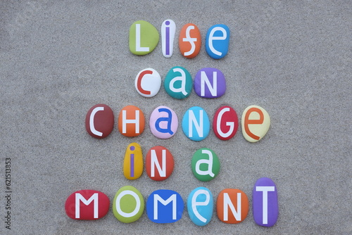 Life can change in a moment, life quote text composed with hand painted multi colored stone letters over beach sand