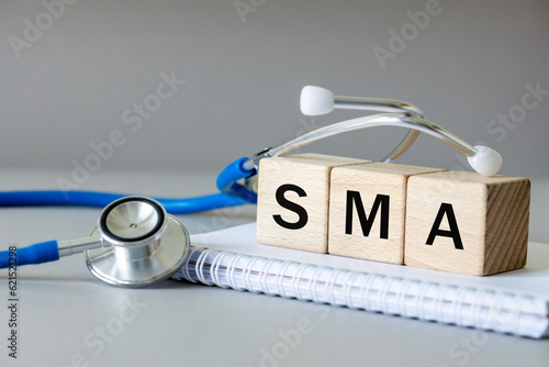 white notebook, Medical stethoscope and wooden blocks with the medical abbreviation SMA for spinal muscular atrophy, severe genetic disease, Beautiful gray background, Medical concept photo