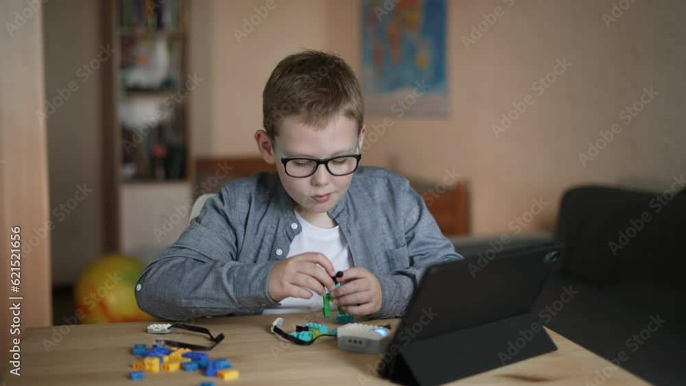 Child in room independently assembles toy from parts constructor using tablet. Boy presses on screen of gadget, shakes head negatively due to incorrect assembly of model, real time. Child in room independently assembles toy from parts constructor using tablet. Boy presses on screen of gadget, shakes head negatively due to incorrect assembly of model, real time.