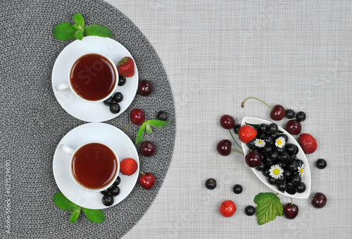 Two cups of tea and fresh summer berries on the plate top view on light color linen fabric background. Healthy food for life concept .Free copy space 