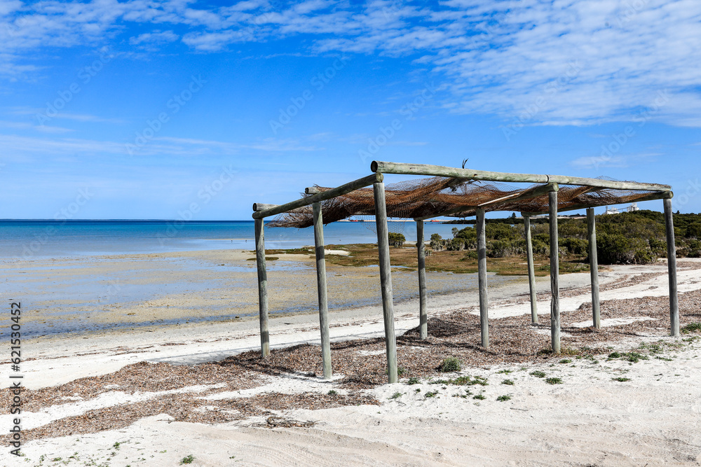 Old rundown timber beach shelter on sandy beach beneath blue sky Old rundown timber beach shelter on sandy beach beneath blue sky