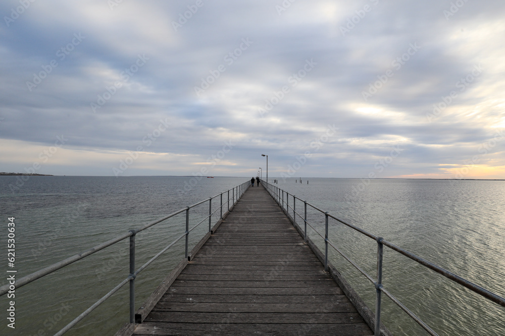 View of jetty leading out to ocean beneath cloudy sky at sunset