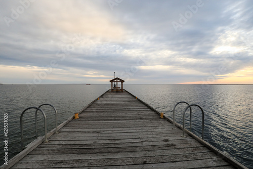 View of jetty leading out to ocean beneath cloudy sky at sunset