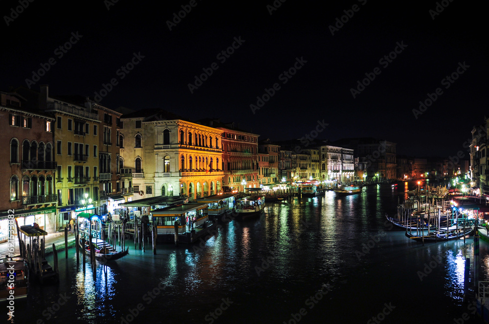 Night view of the Grand Canal in Venice, with many gondolas and boats docked on the banks of the river