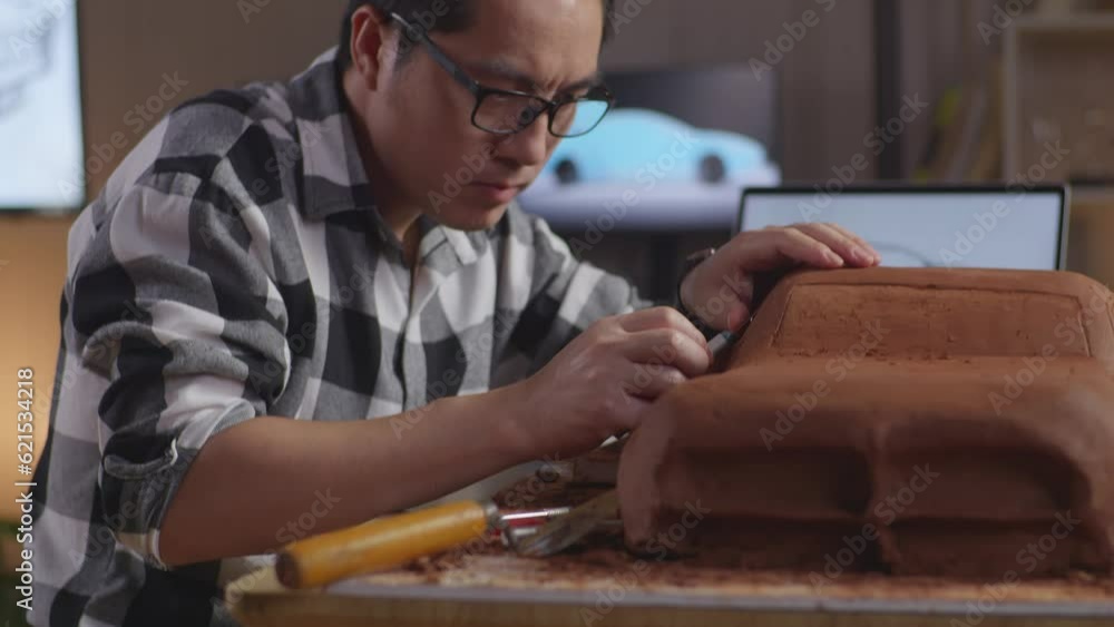 Close Up Of Asian Man Automotive Designer Looking At A Laptop And Using Rake Or Wire To Smooth Out The Surface And Create Details In The Sculpture Of Car Clay In The Studio
Close Up Of Asian Man Automotive Designer Looking At A Laptop And Using Rake Or Wire To Smooth Out The Surface And Create Details In The Sculpture Of Car Clay In The Studio