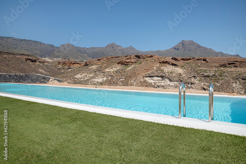 Luxurious long swimming pool overlooking the arid volcanic mountains  surrounded by a perfectly trimmed lawn  tranquil atmosphere of a high-end residential property suited for a lavishing lifestyle