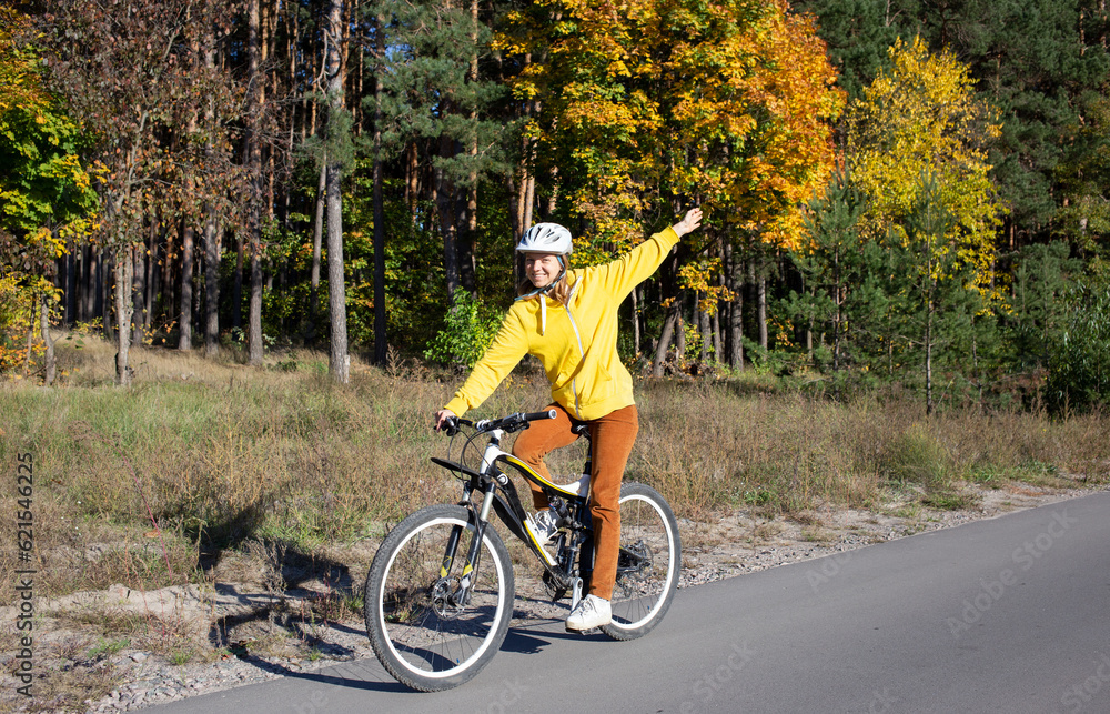 Fototapeta premium young woman on a bicycle rides in an autumn park on a sunny day. Feeling of freedom and joy. Active lifestyle. having fun on an orange autumn background of nature
