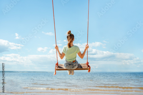 A teenage girl in jeans rides on a swing on the seashore on the beach © KseniaJoyg