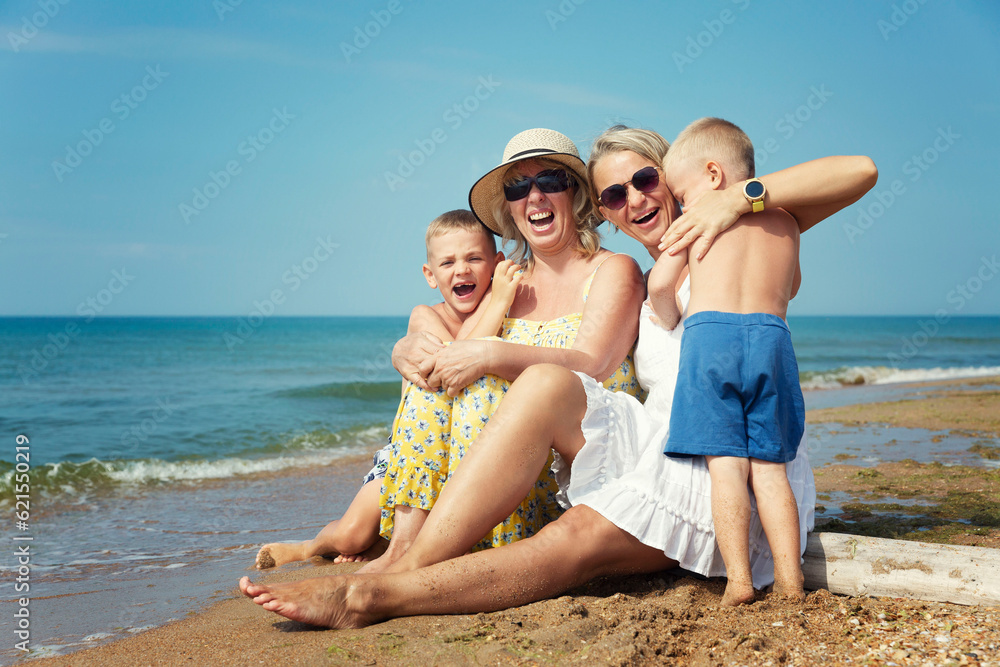 Laughing and hugging family with children on the seashore on a sunny day. Grandmother in a yellow sundress and hat, mother in a white dress and boys sons. Active lifestyle, tourism and travel.