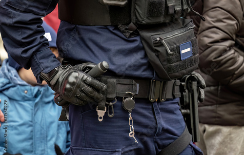 Anonymous police officer holding his hand on his equipment belt, handcuffs, baton, gun, detail, closeup. Emergency response services simple concept, one person, shot up close