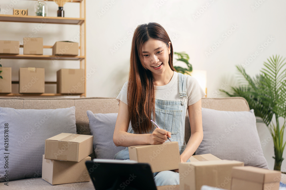 Young entrepreneur is using tablet to checking online orders and writing customer address on cardboard boxes Young entrepreneur is using tablet to checking online orders and writing customer address on cardboard boxes