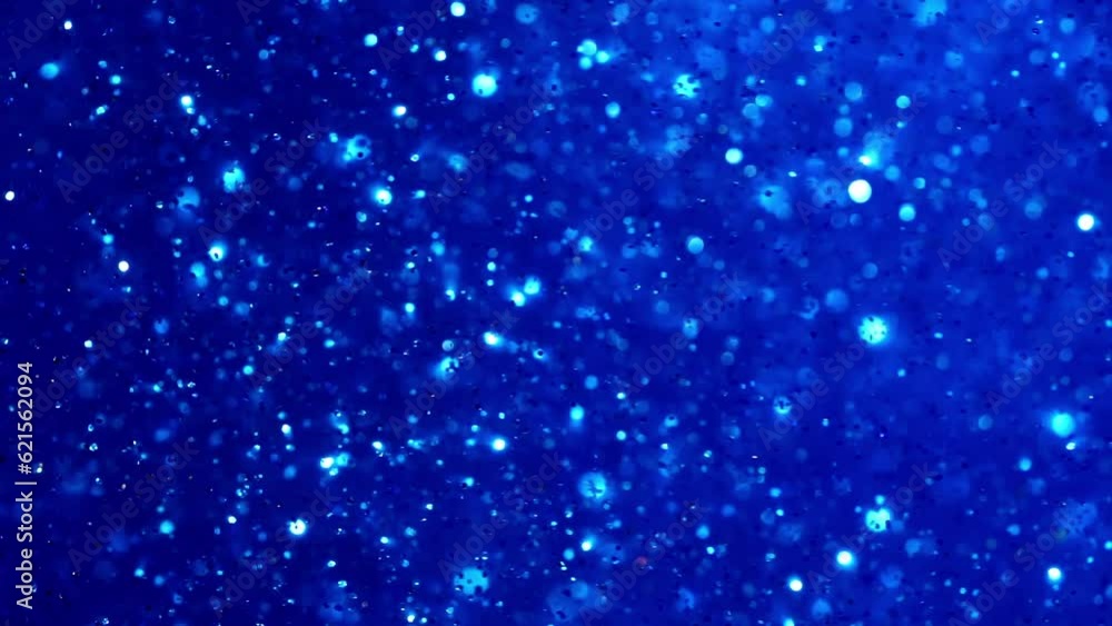 Shiny sparkling particles on a blue background. Movement of white particles and bokeh in a blue fluid with depth of field. A magical underwater galaxy. Abstract Christmas background. Shiny sparkling particles on a blue background. Movement of white particles and bokeh in a blue fluid with depth of field. A magical underwater galaxy. Abstract Christmas background.