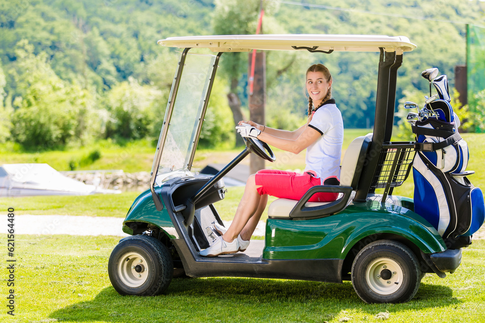 Smiling young woman driving a golf cart along a course while enjoying a round of golf on a sunny day Smiling young woman driving a golf cart along a course while enjoying a round of golf on a sunny day