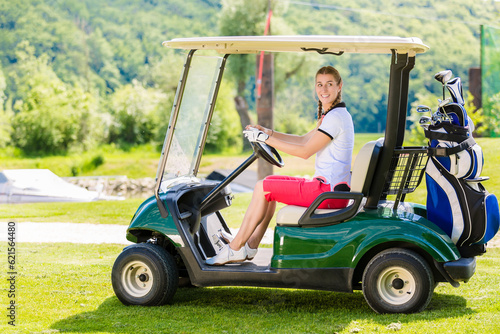 Smiling young woman driving a golf cart along a course while enjoying a round of golf on a sunny day