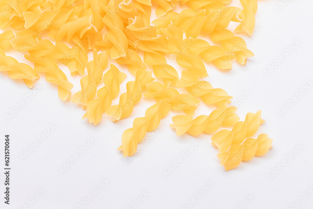 Fototapeta premium A Heap of Uncooked Fusilli Pasta Scattered on White Table. Raw and Dry Macaroni. Unhealthy and Fat Food. Italian Culture