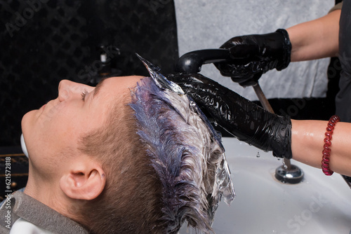 The hands of a girl, a barbershop worker, wearing gloves with rain, water wash off the paint over the sink after dyeing the hair of a client, a guy at work