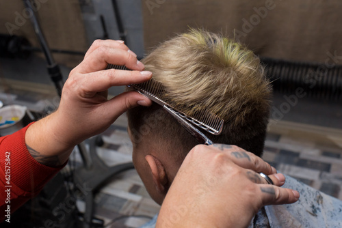 The hands of a professional male hairdresser with scissors and a comb cut the hair of a salon client at work