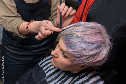 The hands of a girl of an experienced barbershop worker correct a stylish fashionable bob hairstyle with a comb creative color coloring