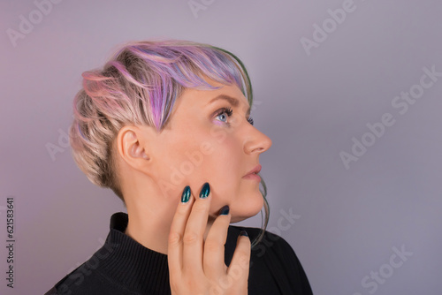 Portrait in profile with a hand near her face a woman of European appearance poses, a pretty adult with a stylish hairstyle, colored coloring and bob on a studio background