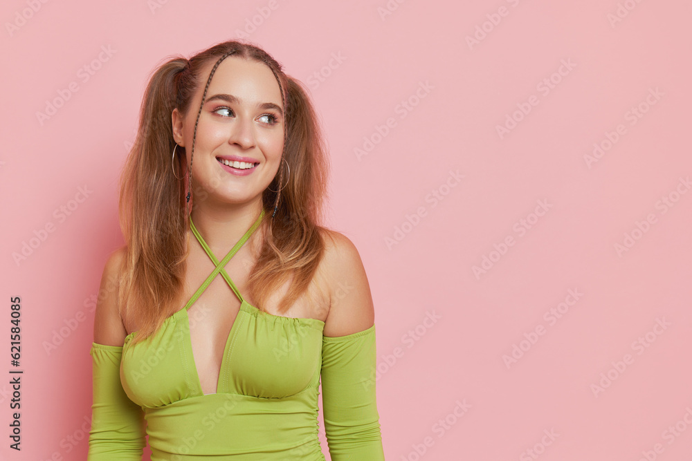 Nice girl with ponytail hairstyle stands against pink background in green longsleeve top,looking aside at empty space, perfect mood concept, copy space Nice girl with ponytail hairstyle stands against pink background in green longsleeve top,looking aside at empty space, perfect mood concept, copy space