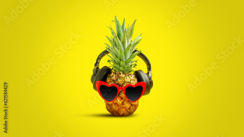 Creative summer layout made of pineapple with red heart shaped sunglasses and black headphones against gradient yellow background. Original pineapple decoration. Minimal summer concept.