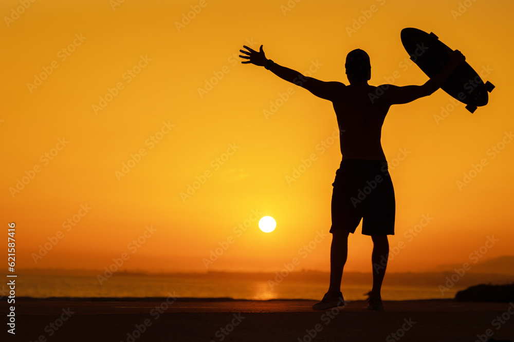 Fototapeta premium Silhouette of a free man holding a skateboard at bright sunset
