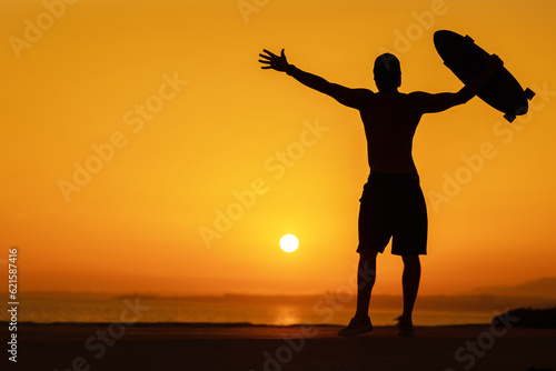Silhouette of a free man holding a skateboard at bright sunset