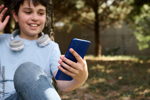 Focus on modern smartphone in hand of a preteen boy talking via video link while resting outdoors. Online communication