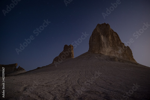 Chalk and limestone remnants in the Kazakh steppe at night against the background of the starry sky and the moon, vertical landforms after weathering in the desert © Denis