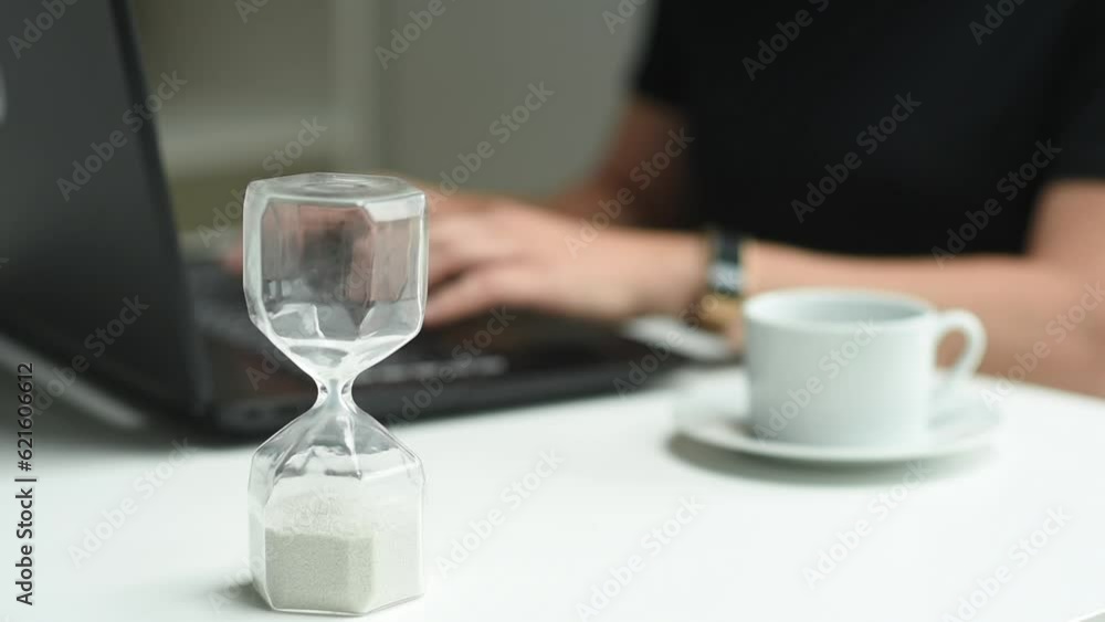 woman is typing on a laptop keyboard. There is an hourglass in the foreground, the background is blurred. Study, business, work, communication via PC woman is typing on a laptop keyboard. There is an hourglass in the foreground, the background is blurred. Study, business, work, communication via PC