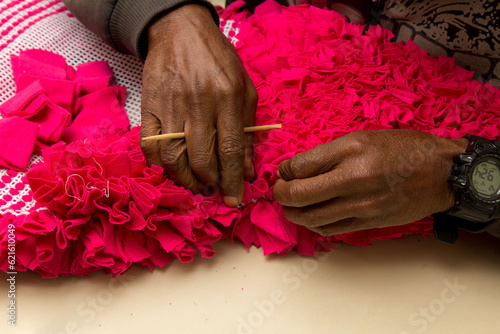 Mãos masculinas tecendo tapete de tecido cor de rosa com palito de madeira. São Paulo, Brasil. photo