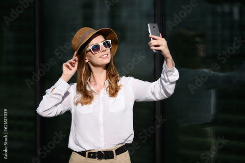 Happy woman in summer clothes, sunglasses, straw hat makes selfie portrait, blogging, video call. Summer, technology
